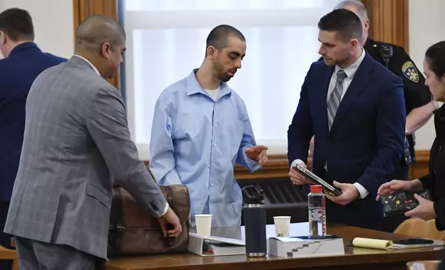 Hadi Matar, center, charged with severely injuring author Salman Rushdie in a 2022 knife attack, speaks to his defense team in Chautauqua County court in Mayville, N.Y., Monday, Feb. 10, 2025. (AP Photo/Adrian Kraus)