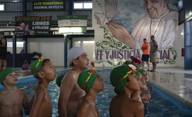 Children listen to a coach during a swimming lesson with a painting of Pope Francis in the background, in San Jose natatorium in Buenos Aires, Argentina, Tuesday, Feb. 18, 2025. (AP Photo/Rodrigo Abd)