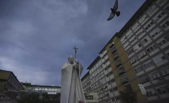 A marble statue of late Pope John Paul II is backdropped by the Agostino Gemelli Polyclinic in Rome, Saturday, Feb. 15, 2025, where Pope Francis was hospitalised Friday after a weeklong bout of bronchitis worsened and is receiving drug therapy for a respiratory tract infection. (AP Photo/Alessandra Tarantino)
