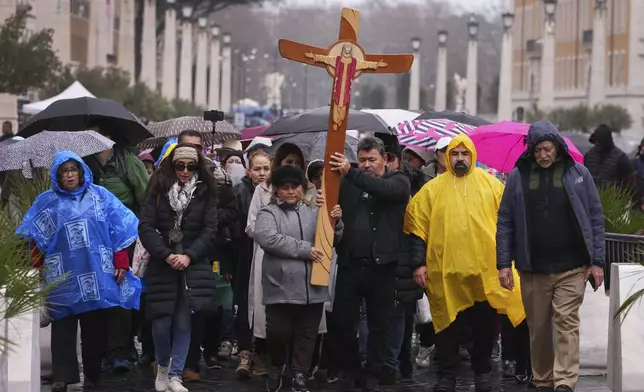 Pilgrims walk through the rain as they carry a cross towards The Vatican in Rome, Italy, Tuesday, Feb. 25, 2025. (AP Photo/Kirsty Wigglesworth)