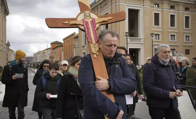 Pilgrims for the jubiliar year 2025 carrying a wooden cricifix arrive in St. Peter's Square at The Vatican, Friday, Feb. 14, 2025, hours after Pope Francis was hospitalized to undergo some necessary diagnostic tests and to continue his ongoing treatment for bronchitis. (AP Photo/Alessandra Tarantino)