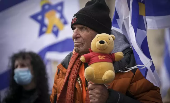 A man holds a teddy bear at the so-called 'Hostages Square' in Tel Aviv, Israel, Thursday, Feb. 20, 2025, after the bodies of four Israeli hostages, including a mother and her two children, were handed over by Palestinian militant groups to the Red Cross in Gaza. (AP Photo/Oded Balilty)