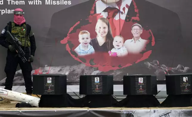 A militant stands next to the coffins containing the bodies of hostages, from right to left, Shiri Bibas, her two children, Ariel and Kfir and Oded Lifshitz, who was 83 when he was abducted before their are handed over to the Red Cross in Khan Younis, southern Gaza Strip, Thursday, Feb. 20, 2025. (AP Photo/Abdel Kareem Hana)
