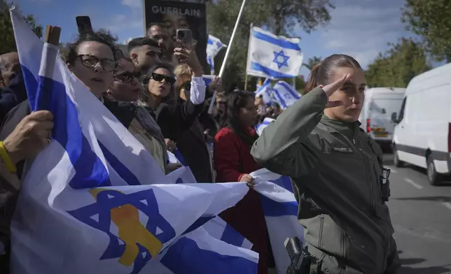 An Israeli border policewoman salutes as a convoy carrying the coffins of four Israeli hostages, including a mother and her two children, arrives at the Abu Kabir Forensic Institute in Tel Aviv, Israel, Thursday Feb. 20, 2025 after the bodies were handed over by Palestinian militant groups in Gaza.(AP Photo/Ohad Zwigenberg)