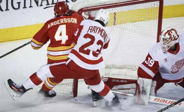 Detroit Red Wings' Lucas Raymond (23) checks Calgary Flames' Rasmus Andersson (4) into the goal post as goalie Cam Talbot looks during the first period of the NHL hockey game against the Calgary Flames, in Calgary, Alberta, Saturday, Feb. 1, 2025. (Jeff McIntosh/The Canadian Press via AP)