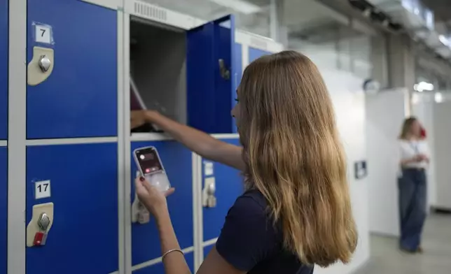 A student stores her mobile phone in a locker at Porto Seguro School in Sao Paulo, Thursday, Feb. 6, 2025, before heading to class under a new law restricting their use in schools. (AP Photo/Andre Penner)