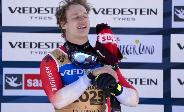 Switzerland's Marco Odermatt listens to the national anthem on the podium after winning the gold medal in a men's Super-G, at the Alpine Ski World Championships, in Saalbach-Hinterglemm, Austria, Friday, Feb. 7, 2025. (AP Photo/Giovanni Auletta)