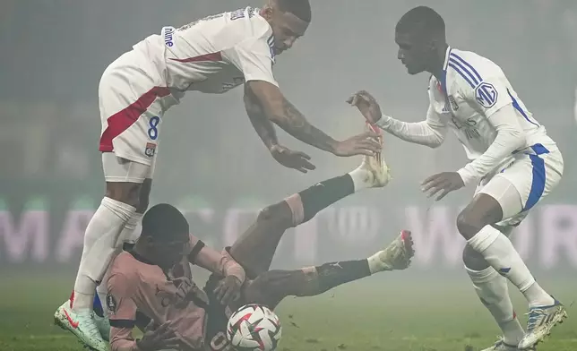 PSG's Ousmane Dembele, center, duels for the ball with Lyon's Corentin Tolisso, left, and Lyon's Clinton Mata during the French League One soccer match between Lyon and Paris Saint-Germain at the Groupama stadium, outside Lyon, France, Sunday, Feb. 23, 2025. (AP Photo/Laurent Cipriani)