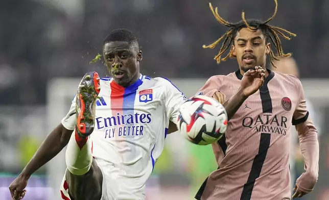 Lyon's Sael Kumbedi, left, duels for the ball with PSG's Bradley Barcola during the French League One soccer match between Lyon and Paris Saint-Germain at the Groupama stadium, outside Lyon, France, Sunday, Feb. 23, 2025. (AP Photo/Laurent Cipriani)