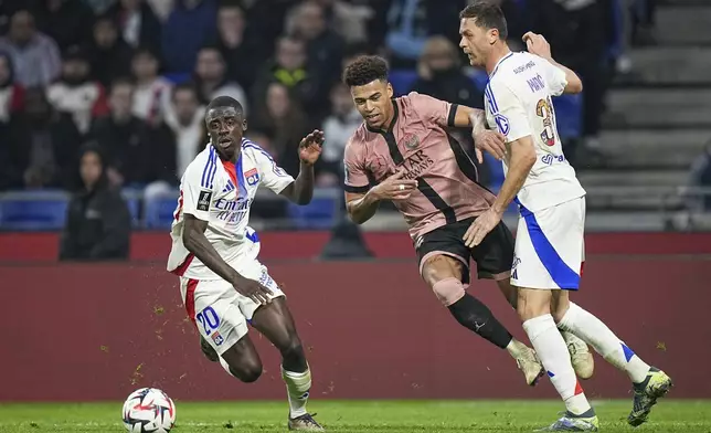 PSG's Desire Doue, center, duels for the ball with Lyon's Nemanja Matic, right, and Lyon's Sael Kumbedi during the French League One soccer match between Lyon and Paris Saint-Germain at the Groupama stadium, outside Lyon, France, Sunday, Feb. 23, 2025. (AP Photo/Laurent Cipriani)