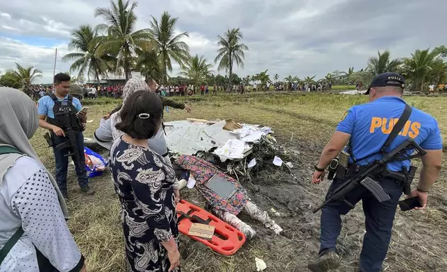 The body of a victim is covered with a blanket as police officers inspect the site where wreckage of airplane is seen in a rice field in Maguindanao del Sur province, Philippines, after officials say a U.S. military-contracted plane has crashed in a rice field in the southern Philippines, killing all four people on board, on Thursday Feb. 6, 2025. (Sam Mala/UGC via AP)
