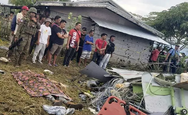 The body of a victim is covered with a blanket as members of security forces stand around wreckage of airplane in a rice field in Maguindanao del Sur province, Philippines, after officials say a U.S. military-contracted plane has crashed in a rice field in the southern Philippines, killing all four people on board, on Thursday Feb. 6, 2025. (Sam Mala/UGC via AP)