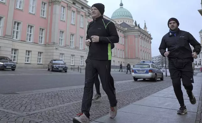 German Chancellor Olaf Scholz, left, jogs in the early morning accompanied by a bodyguard in Potsdam, Germany, Sunday, Feb. 23, 2025. (Michael Kappeler/dpa via AP)
