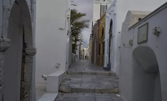 A man walks on an empty street in the town of Oia on the earthquake-struck island of Santorini, Greece, Tuesday, Feb. 4, 2025. (AP Photo/Petros Giannakouris)