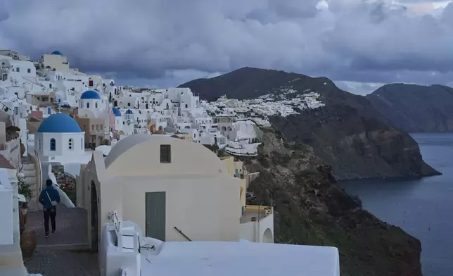 A tourist approaches blue-domed Orthodox churches in the town of Oia on the earthquake-struck island of Santorini, Greece, Tuesday, Feb. 4, 2025. (AP Photo/Petros Giannakouris)