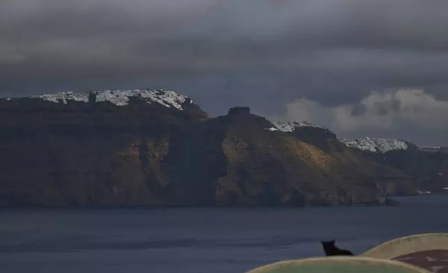A cat sits on a domed roof in the town of Oia on the earthquake-struck island of Santorini, Greece, as the main town of Fira is seen in the background on Tuesday, Feb. 4, 2025. (AP Photo/Petros Giannakouris)