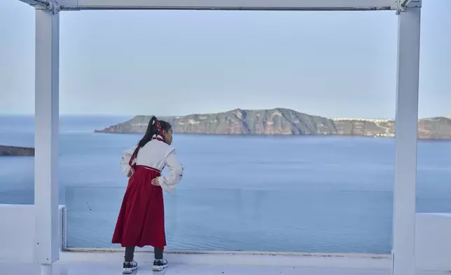 A woman from China looks on from a caldera at Firostefani, as in the background stands the island of Therasia, while authorities are taking emergency measures in response to intense seismic activity on the popular Aegean Sea holiday island of Santorini, southern Greece, Tuesday, Feb. 4, 2025. (AP Photo/Petros Giannakouris)