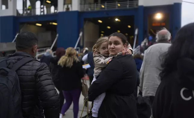 A woman with her child prepare to board a ferry bound for the Greek mainland, in the earthquake-struck island of Santorini, Greece, Tuesday, Feb. 4, 2025. (AP Photo/Petros Giannakouris)
