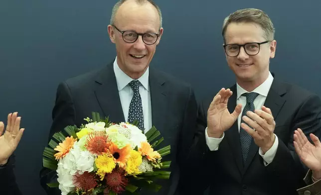Friedrich Merz, left, leader of the Christian Democratic Union (CDU), stand next to Secretary General Carsten Linnemann, right, after he receives flowers at the CDU's headquarters, in Berlin, Germany, Monday, Feb. 24, 2025. (AP Photo/Martin Meissner)