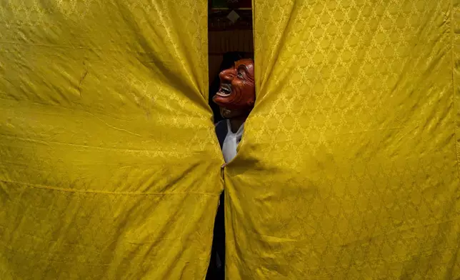 A masked monk stands behind a curtain, assisting a dancer in preparing for a traditional performance during Gyalpo Losar, the Sherpa community's New Year celebration, at Shechen Monastery in Kathmandu, Nepal, on Tuesday, Feb. 25, 2025. (AP Photo/Niranjan Shrestha)