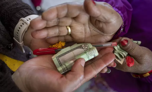 An elderly woman student offers a pen and money as a gift during Saraswati puja, worshiping day of Goddess Saraswati for wisdom and knowledge, celebration at the Ujyalo Community learning center in Kathmandu, Nepal, Feb. 3, 2025. (AP Photo/Niranjan Shrestha)