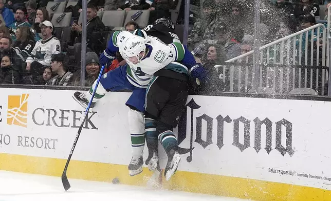 San Jose Sharks defenseman Jack Thompson (26) is checked into the boards by Vancouver Canucks left wing Nils Hoglander (21) during the second period of an NHL hockey game in San Jose, Calif., Thursday, Feb. 6, 2025. (AP Photo/Tony Avelar)