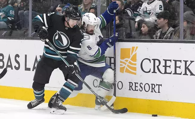 San Jose Sharks defenseman Henry Thrun (3) and Vancouver Canucks right wing Conor Garland (8) battle for the puck during the second period of an NHL hockey game in San Jose, Calif., Thursday, Feb. 6, 2025. (AP Photo/Tony Avelar)