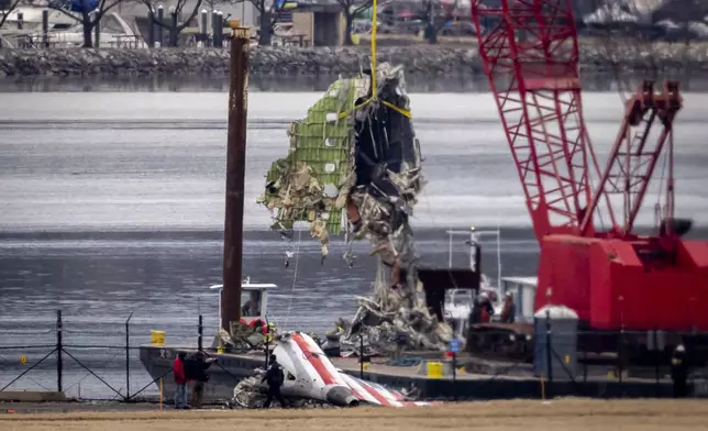 A crane offloads a piece of wreckage from a salvage vessel onto a flatbed truck, near the wreckage site in the Potomac River of a mid-air collision between an American Airlines jet and a Black Hawk helicopter, at Ronald Reagan Washington National Airport, Wednesday, Feb. 5, 2025, in Arlington, Va. (AP Photo/Ben Curtis)