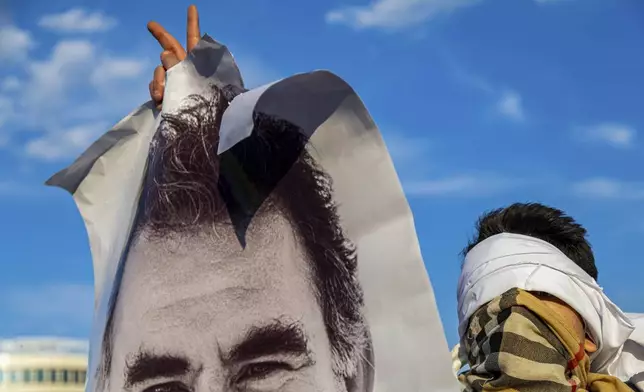 A youngster holds a photograph of the jailed leader of the rebel Kurdistan Workers' Party, or PKK, Abdullah Ocalan as they gather to watch live on a tv screen a Pro-Kurdish Peoples' Equality and Democracy Party, or DEM, delegation members releasing an statement from Ocalan, in Diyarbakir, Turkey, Thursday, Feb. 27, 2025. (AP Photo/Metin Yoksu)