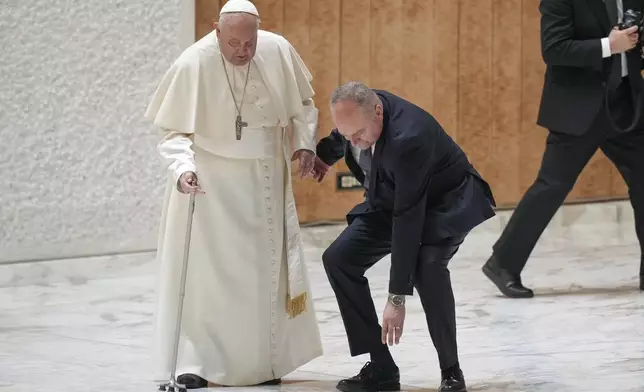 Pope Francis' aide leans down to pick up the the handle of the Pope's walking stick after it snapped as he was arriving for a Jubilee audience in the Pope Paul VI hall at the Vatican, Saturday, Feb. 1, 2025. (AP Photo/Andrew Medichini)