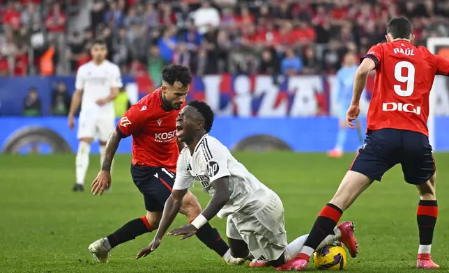 Real Madrid's Vinicius Junior, centre, falls after being tackled during a Spanish La Liga soccer match between Osasuna and Real Madrid at El Sardar stadium in Pamplona, Spain, Saturday, Feb. 15, 2025. (AP Photo/Miguel Oses)