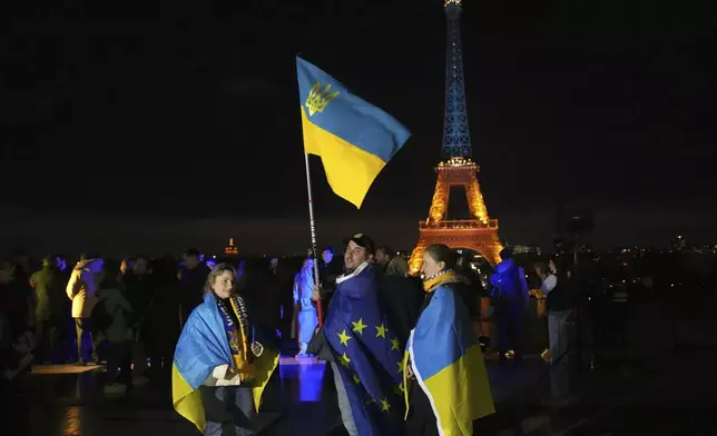 Ukrainians hold Ukrainian and European flag as the Eiffel Tower is illuminated with the colors of Ukraine to mark the third anniversary of Russia's invasion of the country, in Paris, Monday, Feb. 24, 2025. (AP Photo/Christophe Ena)