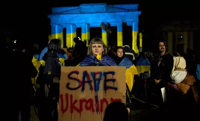 A Protestor holds a placard at the Brandenburg Gate, illuminated in Ukrainian colors, during a demonstration against Russia's war on Ukraine as they mark the third anniversary of the full-scale invasion in Berlin, Monday, Feb. 24, 2025. (AP Photo/Ebrahim Noroozi)