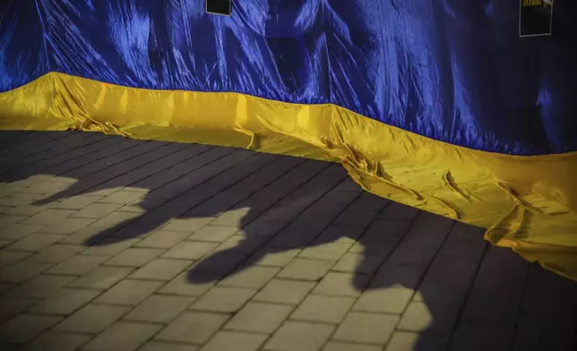 Ukrainian flag and shadows of people are seen during demonstration "Stand with Ukraine" as Bulgarians and Ukrainian refugees express their solidarity with with Ukrainians who have fought for their freedom for three years since the start of the Russian invasion, Sofia, Monday, Feb. 24, 2025. (AP Photo/Valentina Petrova)