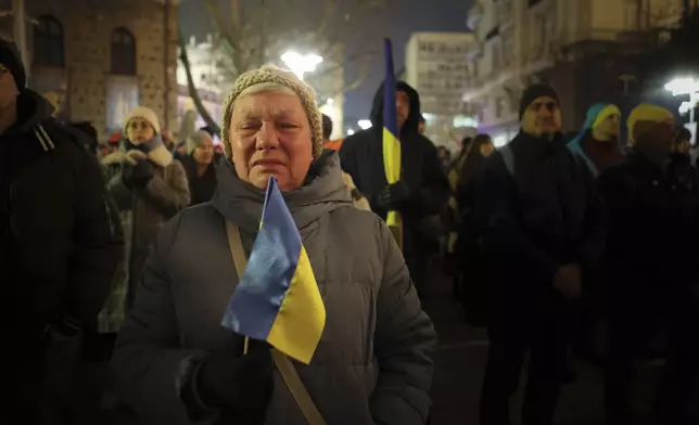 A woman cries as she holds the Ukrainian flag as Bulgarians and Ukrainian refugees express their solidarity with Ukrainians who have fought for their freedom for three years since the start of the Russian invasion, Sofia, Monday, Feb. 24, 2025. (AP Photo/Valentina Petrova)