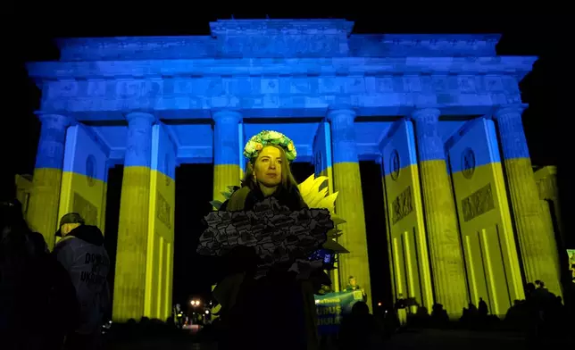 Protesters arrive at the Brandenburg Gate, illuminated in Ukrainian colors, during a demonstration against Russia's war on Ukraine as they mark the third anniversary of the full-scale invasion in Berlin, Monday, Feb. 24, 2025. (AP Photo/Ebrahim Noroozi)