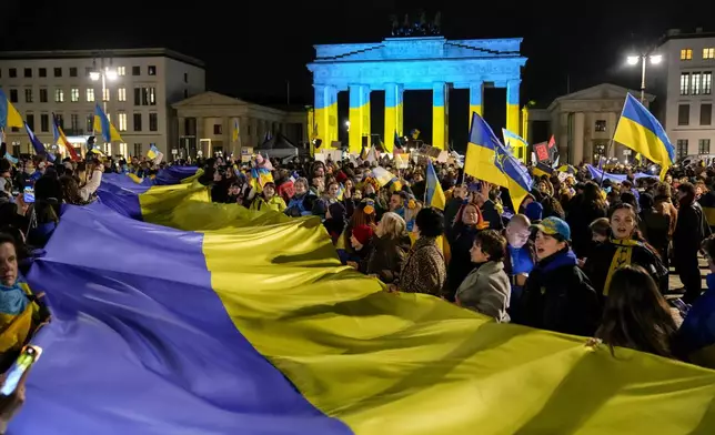Protesters Arrive at the Brandenburg Gate, illuminated in Ukrainian colors, during a demonstration against Russia's war on Ukraine as they mark the third anniversary of the full-scale invasion in Berlin, Monday, Feb. 24, 2025. (AP Photo/Ebrahim Noroozi)