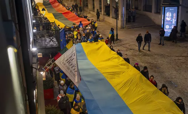 People carry giant Ukrainian and Lithuanian flags to mark the third anniversary of Russia's invasion of Ukraine, in Vilnius, Lithuania, Monday, Feb. 24, 2025. (AP Photo/Mindaugas Kulbis)