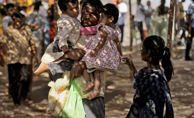 A devotee holds a live chicken while carrying two young children in his arms at the Lingamanthula Swamy temple during a Hindu pilgrimage called the Peddagattu Jatara, in Suryapet, Telangana state, India, Sunday, Feb. 16, 2025. (AP Photo /Mahesh Kumar A.)