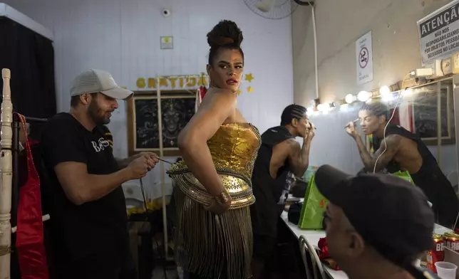 Transgender woman Alessandra Salazary, 31, gets help from her boyfriend with her dress before hosting a Carnival contest show in Rio de Janeiro, Saturday, Feb. 15, 2025. (AP Photo/Silvia Izquierdo