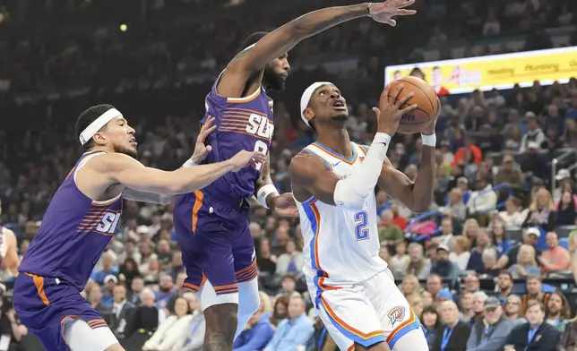 Oklahoma City Thunder guard Shai Gilgeous-Alexander, right, drives past Phoenix Suns forward Royce O'Neale, middle and guard Devin Booker, left, during the first half of an NBA basketball game, Wednesday, Feb. 5, 2025, in Oklahoma City. (AP Photo/Kyle Phillips)