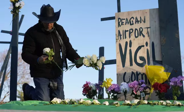 Roberto Marquez, of Dallas, places flowers at a memorial for the 67 victims of a midair collision between an Army helicopter and an American Airlines flight from Kansas near the Ronald Reagan Washington National Airport, Saturday, Feb. 1, 2025, in Arlington, Va. (AP Photo/Carolyn Kaster)