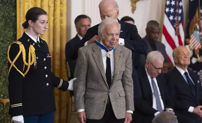 FILE - Army Capt. Rebecca M. Lobach, from left, of Durham, N.C., escorts fashion designer Ralph Lauren as President Joe Biden presents Lauren with the Presidential Medal of Freedom in the East Room of the White House, Jan. 4, 2025, in Washington. (AP Photo/Manuel Balce Ceneta, File)