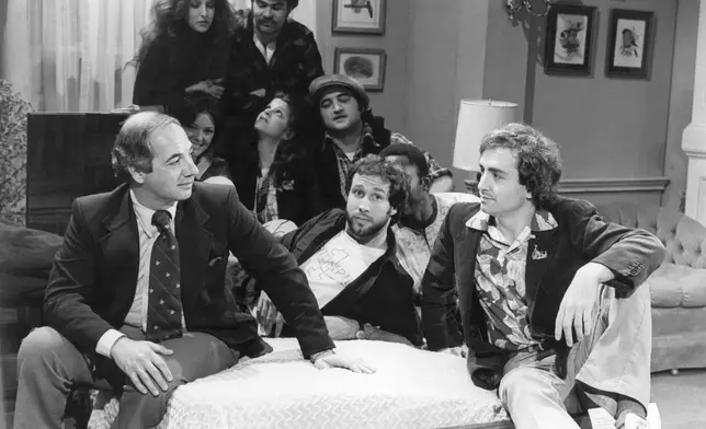 FILE - White House Press Secretary Ron Nessen, left, appears on the "Saturday Night Live" set with producer Lorne Michaels, right, and cast members Chevy Chase, foreground center, Laraine Newman, background left, Dan Aykroyd, background right, Jane Curtin, second row from left, Gilda Radner, John Belushi and Garret Morris, partially obscured, on April 17, 1976, in New York. (AP Photo)