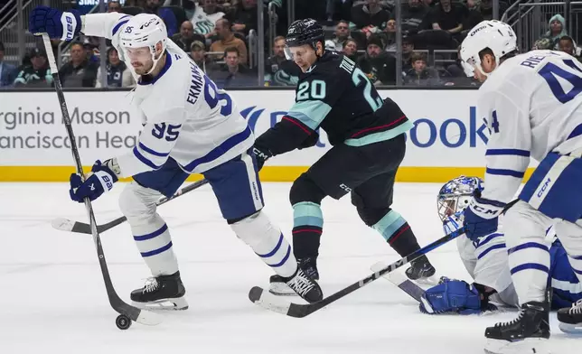 Toronto Maple Leafs defenseman Oliver Ekman-Larsson, left, clears the puck against Seattle Kraken right wing Eeli Tolvanen (20) as Maple Leafs goaltender Anthony Stolarz and defenseman Morgan Rielly, right, look on during the second period of an NHL hockey game Thursday, Feb. 6, 2025, in Seattle. (AP Photo/Lindsey Wasson)
