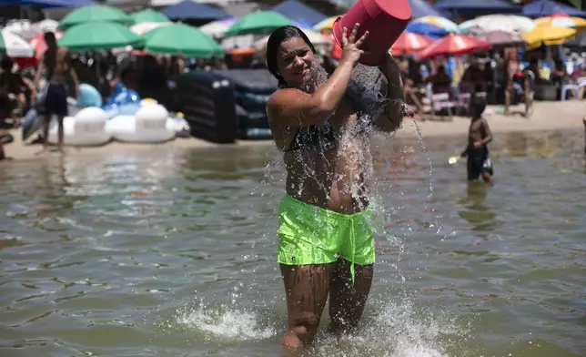 A woman cools herself off with a bucket of water at the Piscinao de Ramos artificial beach during summer in Rio de Janeiro, Sunday, Feb. 16, 2025. (AP Photo/Bruna Prado)