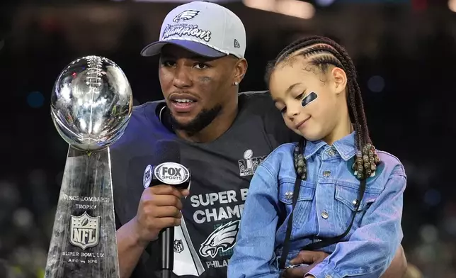 Philadelphia Eagles running back Saquon Barkley holds his daughter Jada while being interviewed after the NFL Super Bowl 59 football game against the Kansas City Chiefs, Sunday, Feb. 9, 2025, in New Orleans. (AP Photo/Brynn Anderson)