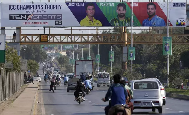 Cars and motorcyclists drive past a billboard depicting portraits of the various cricketers in preparation for ICC Champions Trophy 2025, installed on a pedestrian bridge on a road in Karachi, Pakistan, Sunday, Feb. 16, 2025. (AP Photo/Fareed Khan)