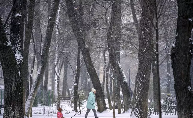 A woman pulls a child on a sled during a snowfall in Bucharest, Romania, Sunday, Feb. 16, 2025. (AP Photo/Andreea Alexandru)