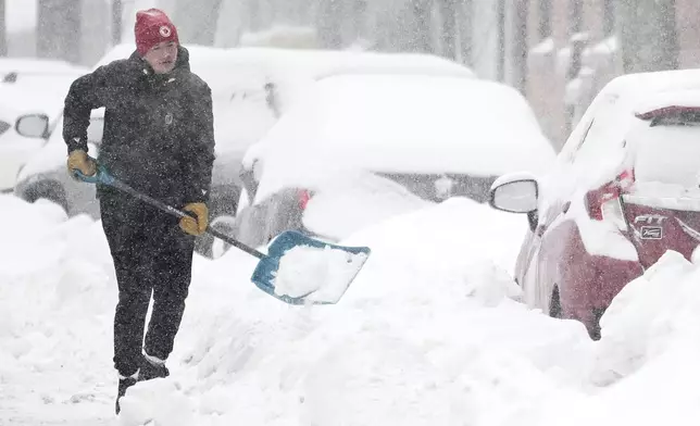 A person clears snow from around a car during a snowstorm in Montreal, Sunday, Feb. 16, 2025. (Graham Hughes/The Canadian Press via AP)